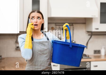 Scared young woman calling plumber holding bucket Stock Photo