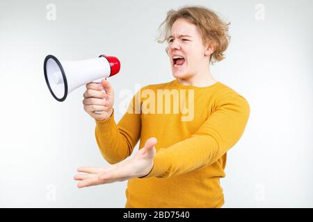 blond wavy guy shouting news into a loudspeaker on a white studio background Stock Photo