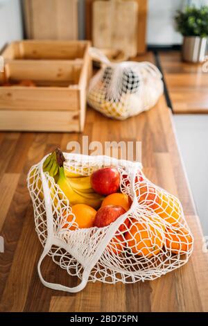Some fruits and vegetables in a reusable organic cotton mesh bag on wooden background. Zero waste, plastic free concept. Sustainable lifestyle. Stock Photo