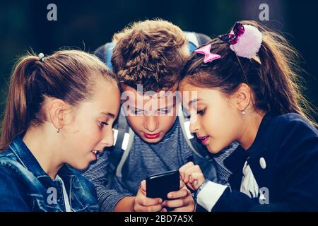 Group of friends hang out after school and using smart phone together while sitting on the bench in the park. Stock Photo
