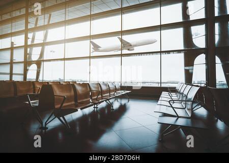 A dark interior of a waiting hall near departure gates of a modern airport terminal with rows of empty wooden armchairs on a tiled floor and taking of Stock Photo