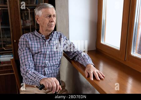 A handsome elderly man, 80 years old, sits at home and looks out the window. Stock Photo