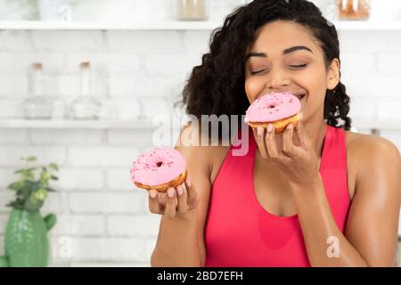 Happy Slim Afro Girl Eating Two Doughnuts Stock Photo