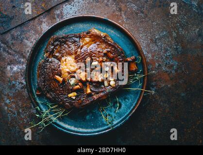 Juicy grilled beef ribeye steak with mushrooms, onion and thyme in a plate top view American food Stock Photo