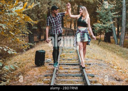 A young couple of lovers missed the train. Walking on the rails in the autumn forest waiting for the next train. Stock Photo