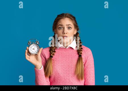 Frightened girl holding alarm clock in hand Stock Photo