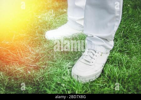 Male feet in white shoes on green grass. White jeans. Stock Photo
