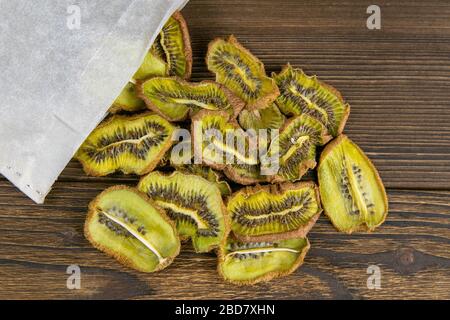 A photo of dried Kiwi fallen out of a kraft paper bag on a dark wooden boards texture Stock Photo