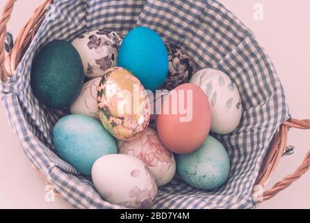 Wicker basket with colored Easter eggs on a light background, close-up Stock Photo