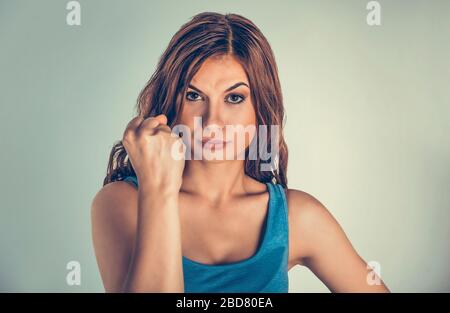 Closeup portrait serious unhappy, irritated, angry, annoyed, displeased young woman, lady, girl showing fist isolated green wall background. Negative Stock Photo