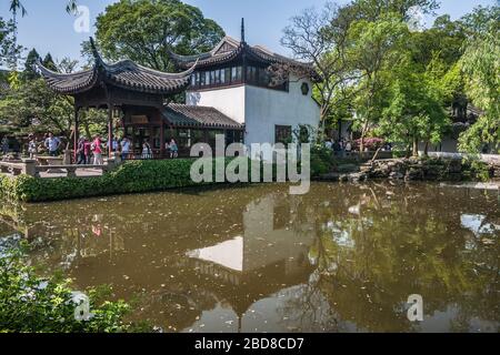 Suzhou China - May 3, 2010: Humble Administrators Garden. Brown-white structure in Chinese architecture set in pond surrounded by green foliage under Stock Photo