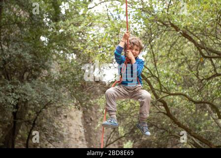 Four year old smily toddler plays hanging from a climbing rope Stock Photo