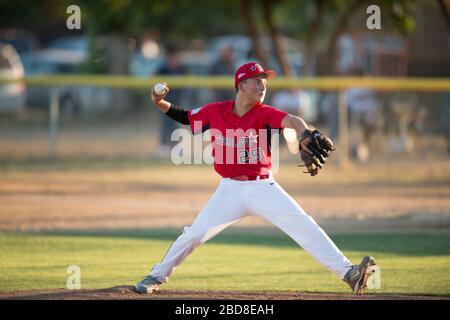 teen baseball pitcher in red uniform in full wind up on the mound Stock Photo