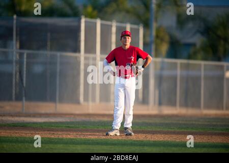 Teen baseball player in red uniform standing in the infield Stock Photo