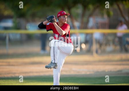 teen baseball pitcher in red uniform in full wind up on the mound Stock Photo
