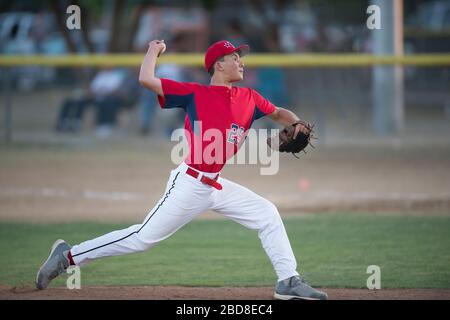 teen baseball player pitcher in red uniform in full wind up on the mound Stock Photo