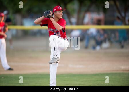 teen baseball pitcher in red uniform in full wind up on the mound Stock Photo