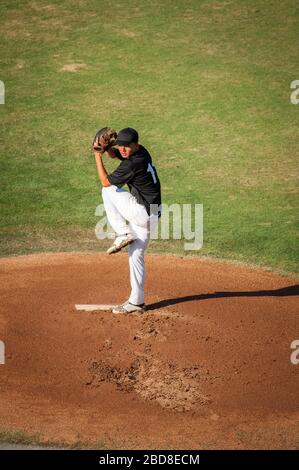 Teen baseball player in black and white uniform in full wind up on the mound Stock Photo