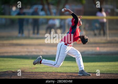 teen baseball player pitching in red uniform in wind up on the mound Stock Photo