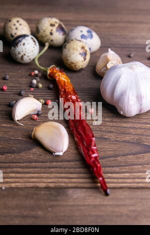 Spicy, garlic, hot red peppers, quail eggs on a dark wooden background. Stock Photo
