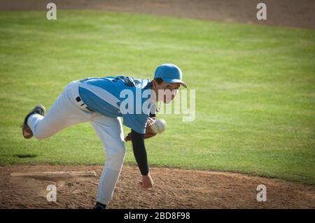 Pitcher in light blue and white jersey during wind up on a baseball field. Stock Photo