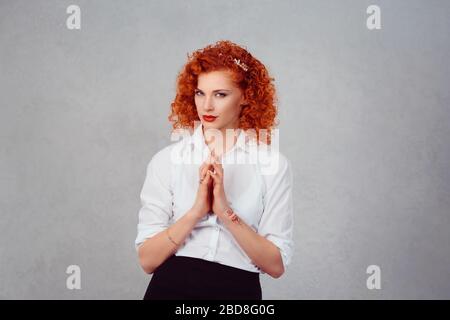 Plotting. Closeup portrait sneaky, sly, scheming young redhead woman plotting revenge plan, prankster isolated on gray wall background. Negative human Stock Photo