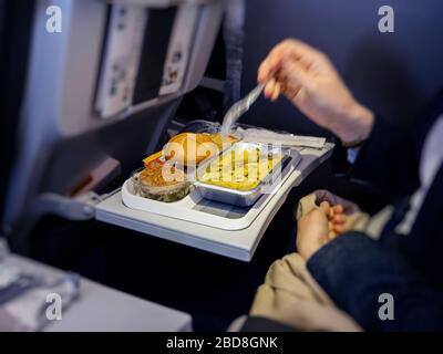 Side view of woman eating delicious meal in modern aircraft economy business class during long transatlantic flight - pasta, meat and bread Stock Photo