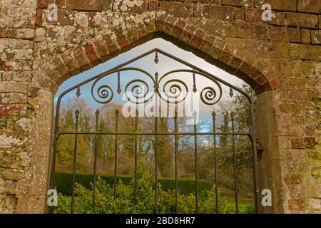 Wrought iron gate entrance to the walled garden with woodland in the backround at Chawton House garden showing bricks and stone in the wall construction Stock Photo