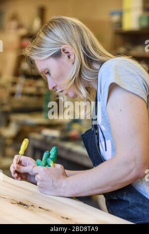 Inside the Wood Industry or Lumber Industry private sector, production of forest products. Female carpenter making slab furniture products, Stock Photo