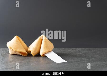 Two fortune cookies rest on a black slate table top with a blank fortune and copy space; landscape view Stock Photo