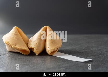 Close-up of two fortune cookies with a blank fortune coming out of it on a black slate background; landscape view Stock Photo