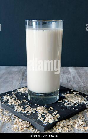 Vegan oat milk or drink in glass with oats strewn around on black tile with black background Stock Photo