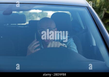 Closeup portrait, young man in blue suit driving in car and checking his phone, then shocked almost about to have traffic accident, isolated interior Stock Photo