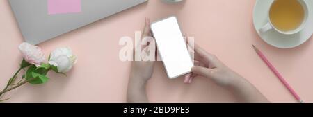 Overhead shot of female university student using smartphone while doing homework with laptop on pink table Stock Photo