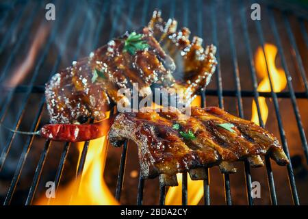 Portions of spicy pork ribs seasoned with herbs on a BBQ grill sizzling over the hot coals in close up Stock Photo