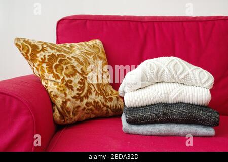 Closeup shot of warm sweaters and cushion on red sofa in living room Stock Photo