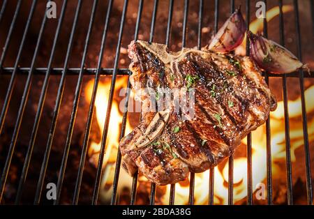 Bone-in rib eye steak seasoned with herbs and spices grilling ver a hot BBQ fire in a view from above with copy space Stock Photo