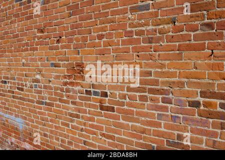 Antique red and brown exterior clay brick wall texture background, with rugged deterioration, photographed in sunlight, Stock Photo