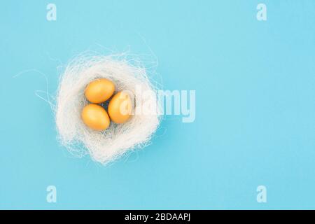 Decorative bird nest with golden easter eggs on blue pastel background. Easter concept. Flat lay. Stock Photo