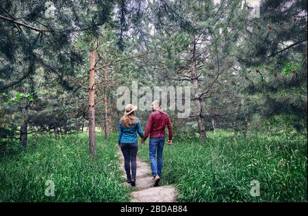 Young hipster couple in checkered shirt holding by hands and walking in the pine tree forest. Love in the nature. Stock Photo