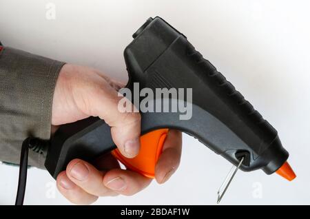 Hand holds an electric glue gun. Man in gray protective clothing. Using a hand tool. Close-up. Selective focus. Stock Photo