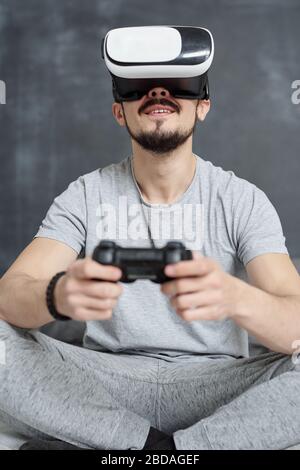 Below view of bearded man in homewear excited about virtual video game using joystick in VR goggles Stock Photo