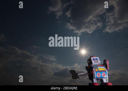 Vintage toy robot with sky behind. Artificial intelligence concept. Dark ambient. Stock Photo