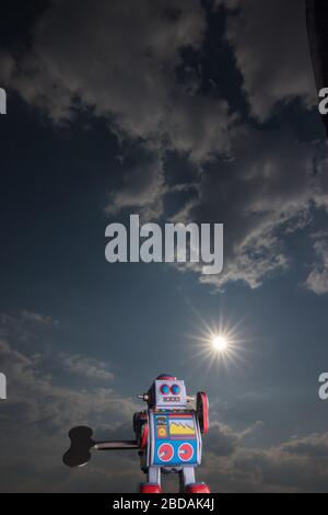 Vintage toy robot with sky behind. Artificial intelligence concept. Dark ambient. Stock Photo