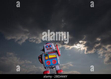 Vintage toy robot with sky behind. Artificial intelligence concept. Dark ambient. Stock Photo