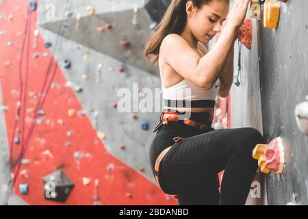 Sportswoman climber moving up on steep rock, climbing on artificial wall indoors. Extreme sports and bouldering concept Stock Photo