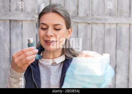 Beautiful young woman holding asthma inhaler and surgical mask outdoor Stock Photo
