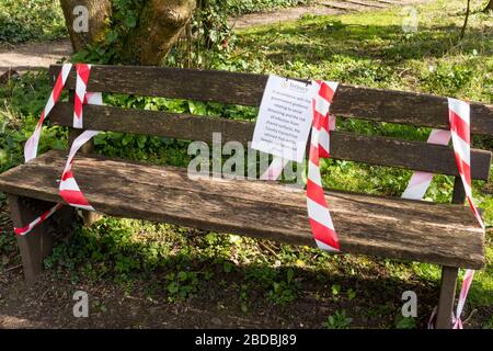 Park bench with sign not to sit on and white and red warning tape, Tetbury, Gloucestershire, UK