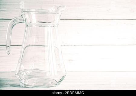 An empty glass carafe for water stands on a white wooden background Stock Photo