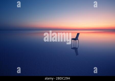 Chair among smooth water of lake at sunset. The concept of solitude and unity with nature. A chair stands in the water of the Salt Lake Ace. Anatolia, Stock Photo